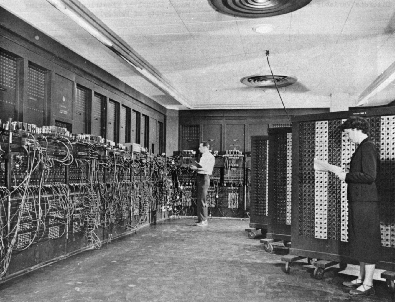Two operators programming the ENIAC computer by setting cables and switches on its large panels